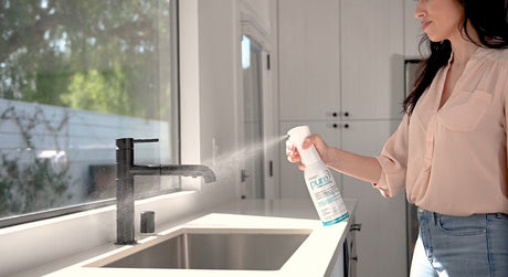 Woman using PURE Hard Surface disinfectant spray in a modern kitchen, demonstrating non-toxic, food-safe cleaning for residential and commercial use.