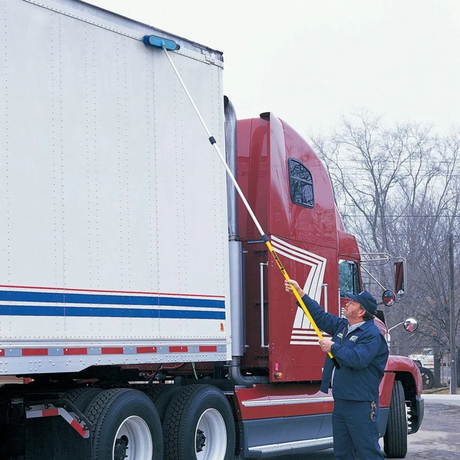 Man cleaning a semi truck with a long-handled brush and extension pole